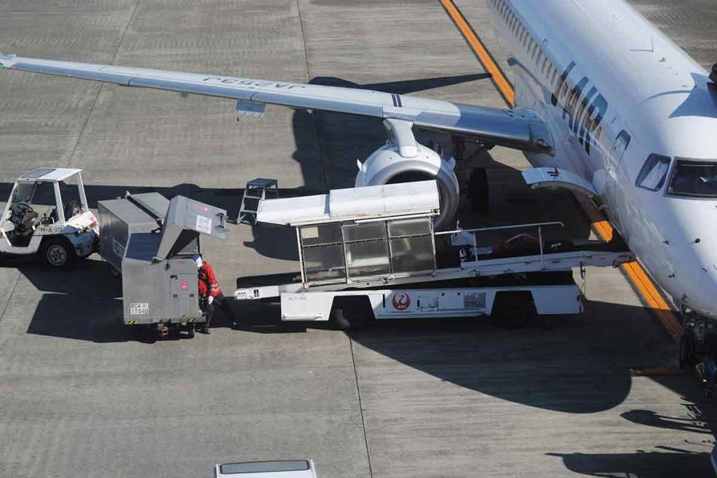 Large white cargo airplane on airport tarmac being loaded with freight containers by ground crew and machinery