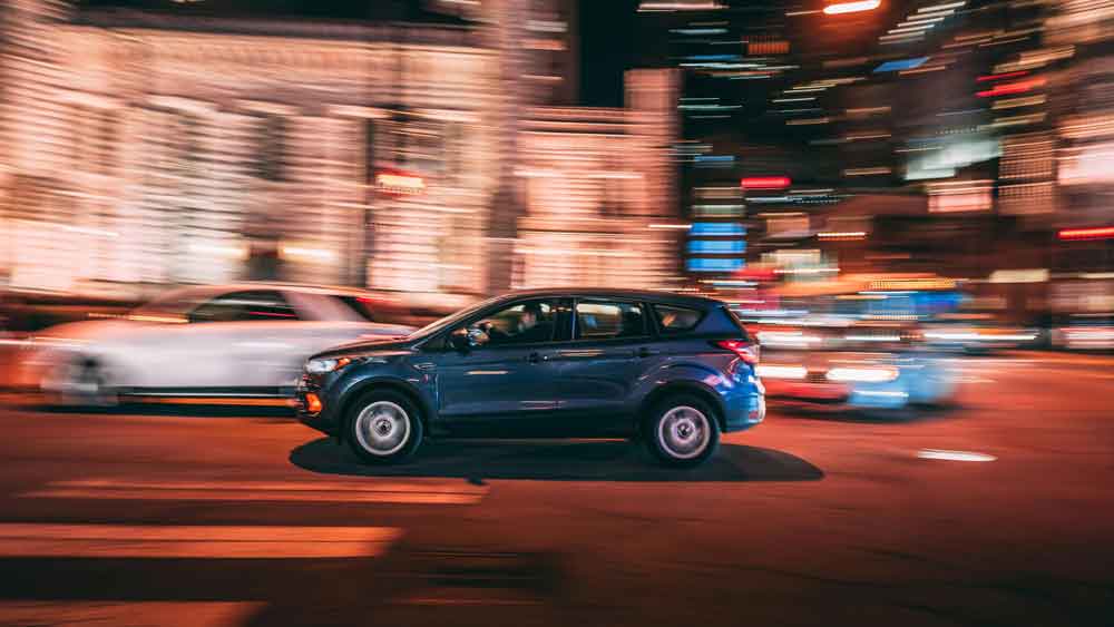 Dark blue SUV in motion on a city street at night, reflecting comfortable and spacious travel for luggage.
