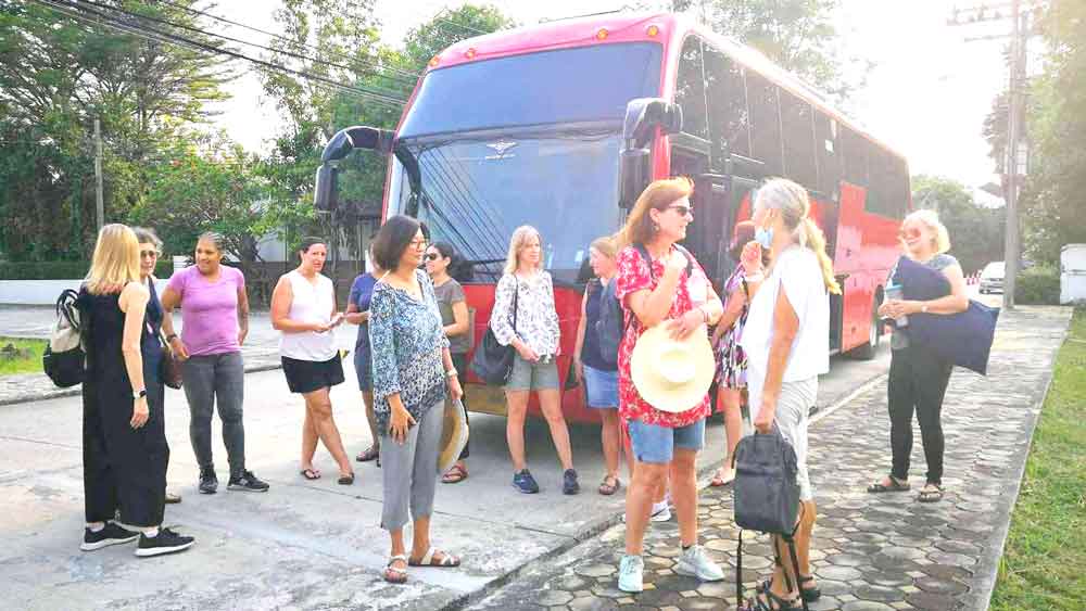 A group of women standing by a red mini bus on a sunny day, ready for comfortable group tour travel.