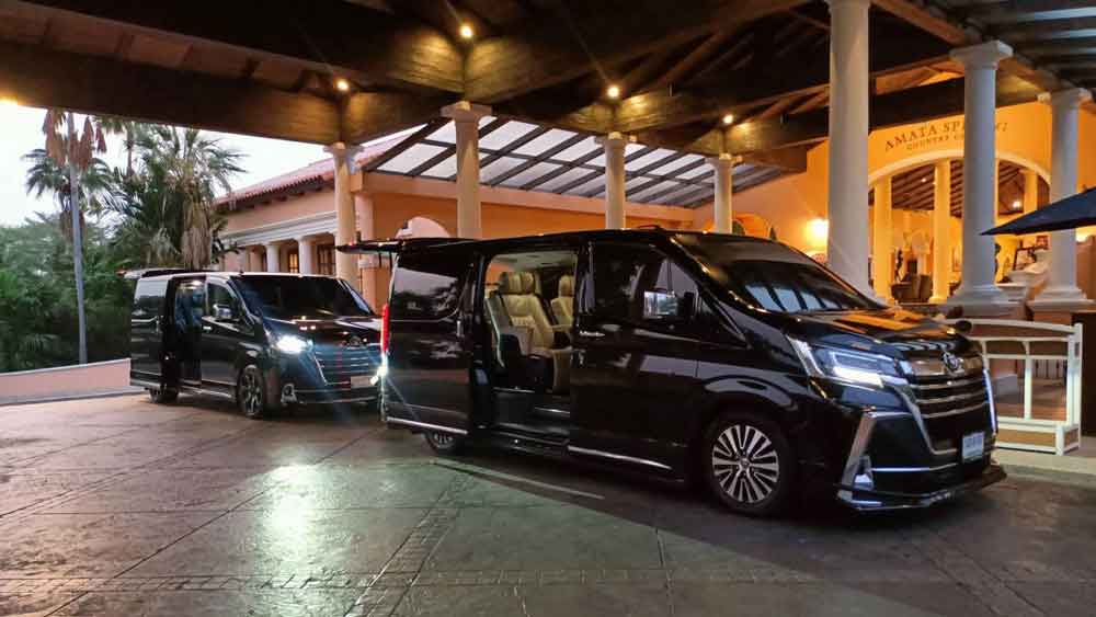 Two black luxury vans with open doors parked at a hotel entrance at dusk, reflecting ready group transport service.